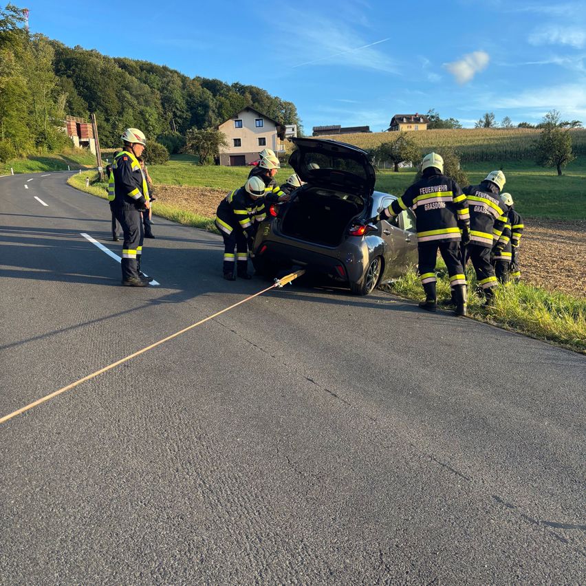 Feuerwehrleute ziehen ein Auto mit einem Seil von der Straße, wobei eine Person von vorne führt.
