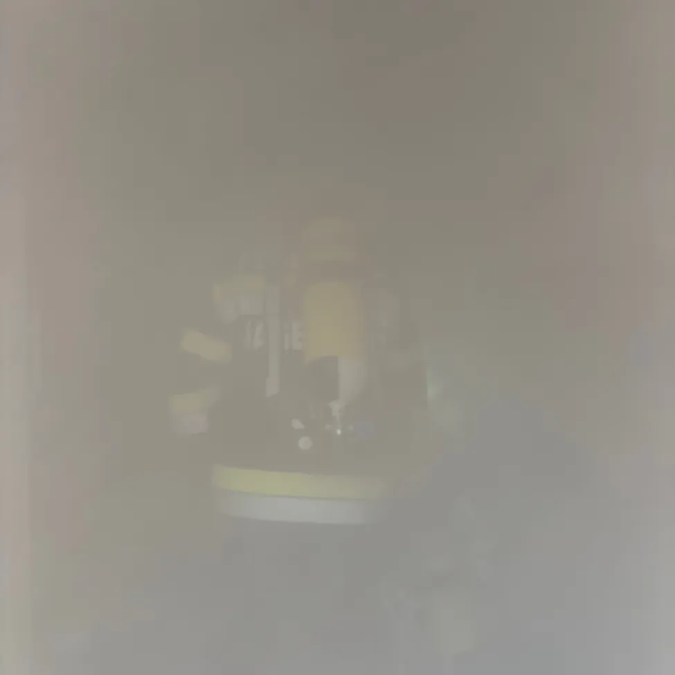 Ein verschwommenes Bild eines gelben und weißen Objekts, möglicherweise ein Feuerlöscher, mit einer Person in einem gelben Jackett im Vordergrund.