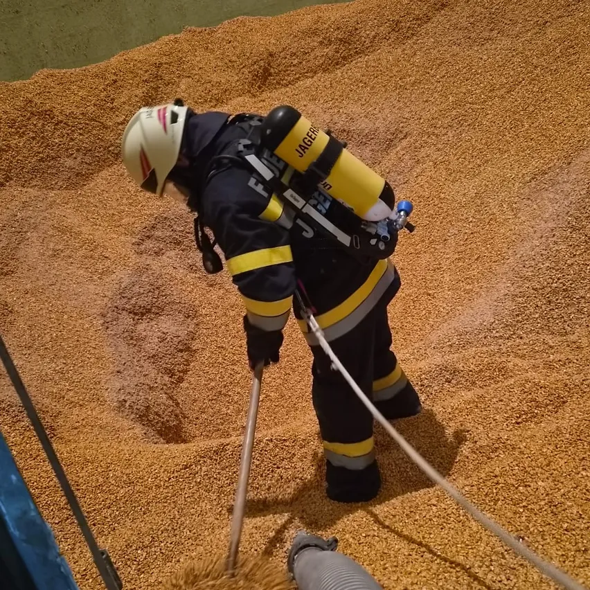 Ein Feuerwehrmann in voller Ausrüstung, einschließlich Helm, benutzt ein Werkzeug, um in einem Getreidehaufen zu graben.