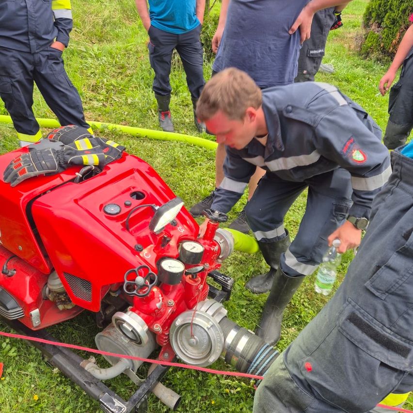 Ein Feuerwehrmann inspiziert einen roten Motor mit einer Gruppe anderer auf einem Grasfeld.