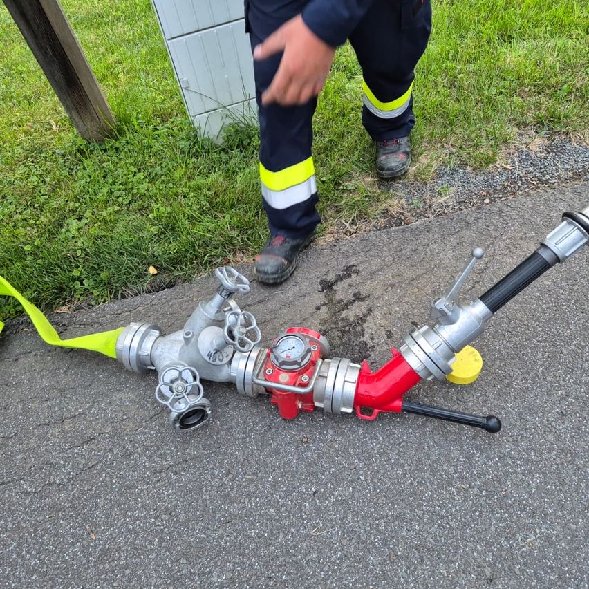 Ein Feuerwehrmann steht neben einem Hydranten, dessen Schlauch auf dem Boden liegt.