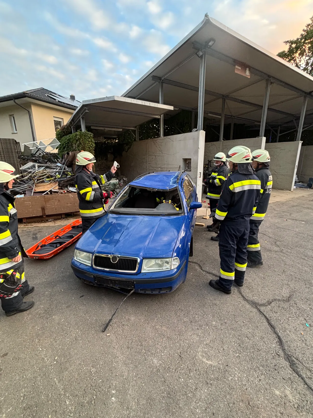Feuerwehrleute in Uniform inspizieren ein beschädigtes blaues Auto auf einem Parkplatz.