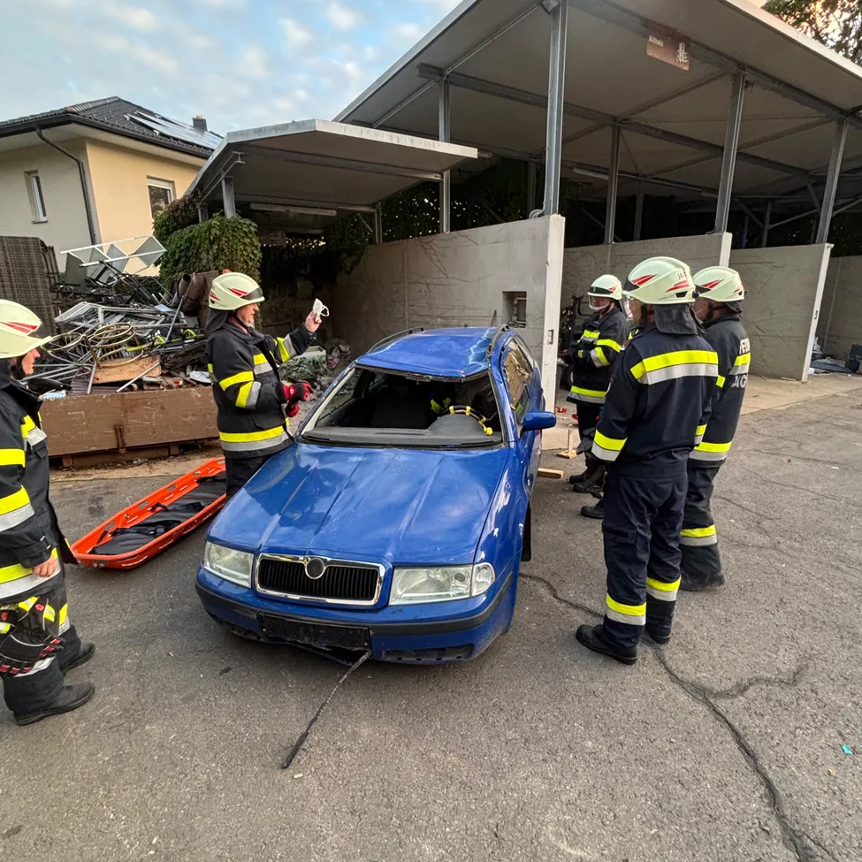 Feuerwehrleute in Uniform inspizieren ein beschädigtes blaues Auto auf einem Parkplatz.
