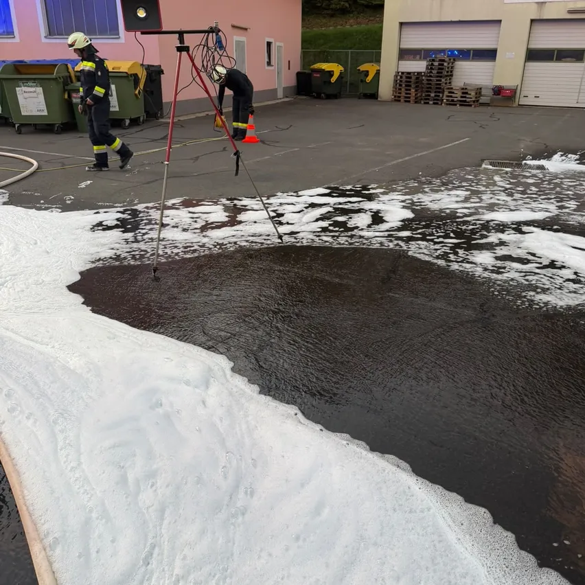 Zwei Feuerwehrleute in Uniform arbeiten auf einer nassen Straße, einer benutzt ein Stativ und der andere beugt sich vor.