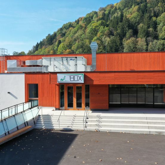 Die Vorderseite einer Kunstgalerie, art BOX, ist aus rotem Holz mit einem Berg im Hintergrund. Es gibt weiße Treppen, die zum Eingang führen.
