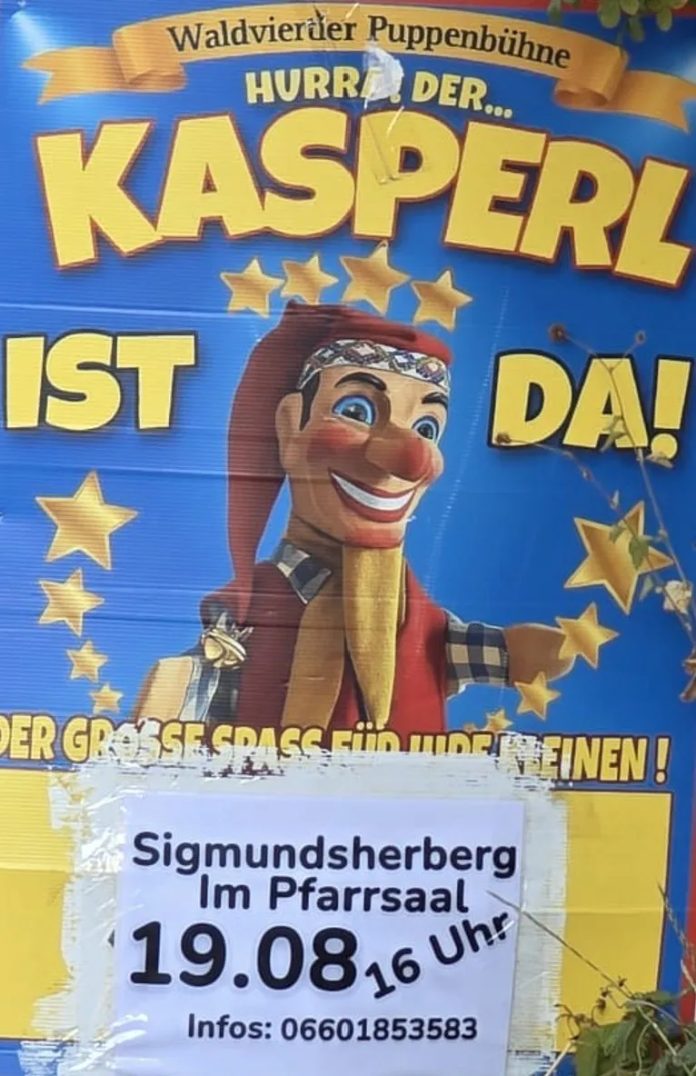 Ein Plakat für eine Puppenshow mit einer Figur namens Kasperl, die fröhlich lächelt und einen roten Hut trägt. Das Plakat hat einen blauen Hintergrund mit gelben Sternen und Text auf Deutsch.