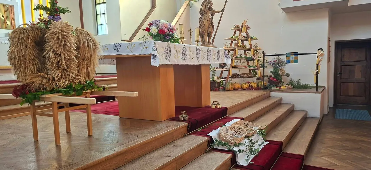 Ein hölzerner Altar mit einer weißen Tischdecke, Blumen und einer Statue einer Person mit einem Speer. Der Altar ist von Treppen und einem hölzernen Geländer umgeben.