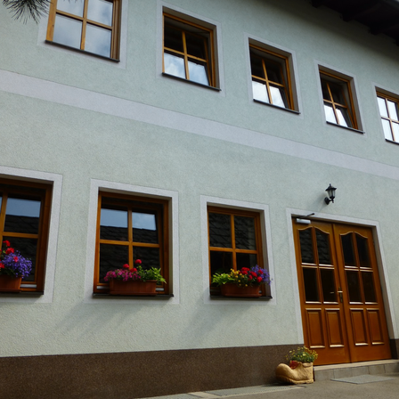 Ein Haus mit weißen Wänden und braunen Verkleidungen hat drei Fenster mit Blumenkästen und eine braune Doppeltür.