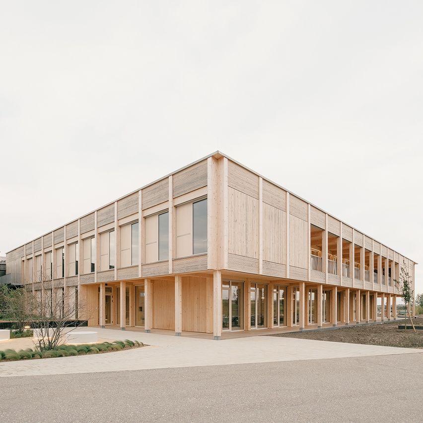 Ein modernes Gebäude mit holzverkleideter Außenfassade, mehreren Glasfenstern und einem gepflasterten Gehweg vor der Fassade.