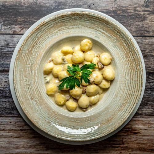 Eine Schüssel mit cremigen Gnocchi und einer grünen Garnierung auf einem Holztisch.