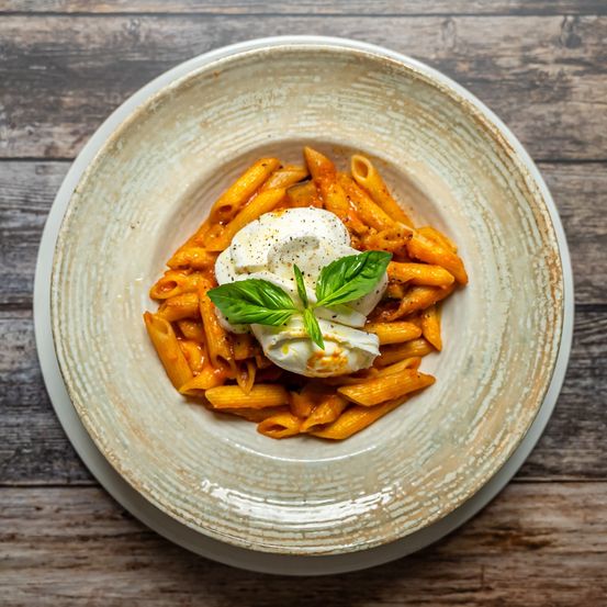 Eine Schüssel mit Tomatensoße und einer Kelle Sahne darauf, garniert mit Basilikumblättern, serviert auf einem Holztisch.