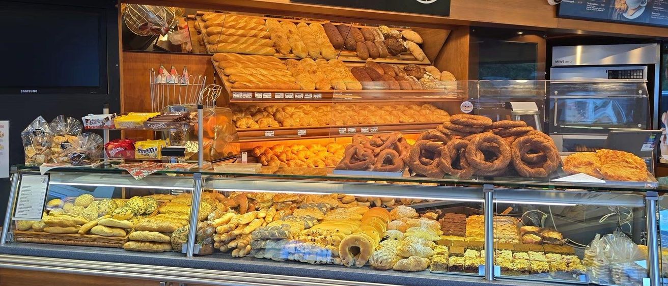 Eine Bäckerei-Auslage mit einer Vielzahl von Broten und Gebäck, darunter Croissants, Baguettes und Donuts, unter einem Schild, das 'BACKEREI HIRT' steht.