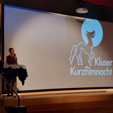 Bild enthält, People, Person, Crowd, Screen, Audience, Projection Screen, Face, White Board, Microphone, Speech