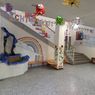 Ein dekorierter Innenraum mit einer Treppe, einer Regenbogenwand und verschiedenen hängenden Dekorationen. Eine kleine Bank und Topfpflanzen stehen auf dem Boden. Die Decke hat hängende Dekorationen und Lichter.