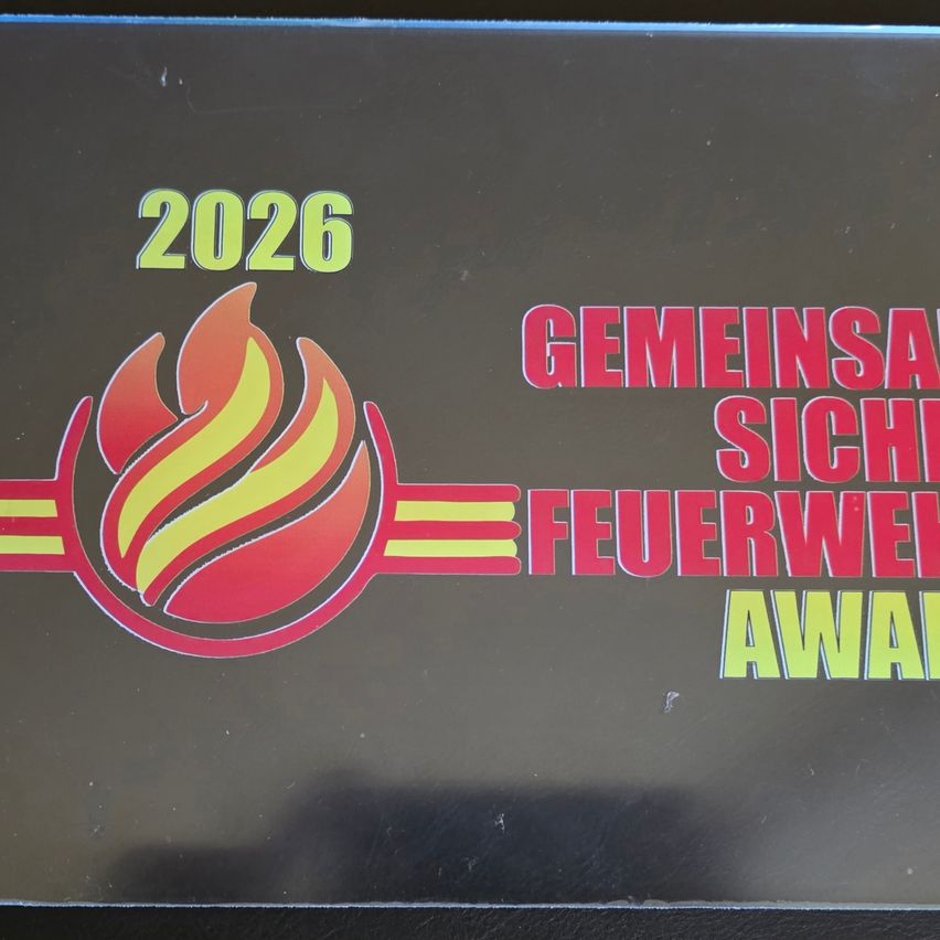 Eine schwarze Plakette mit einem Feuerlogo, die '2026 GEMEINSA SIC FEUERWE AWAR' lautet, wahrscheinlich eine Auszeichnung für gemeinschaftliche Sicherheit für 2026.
