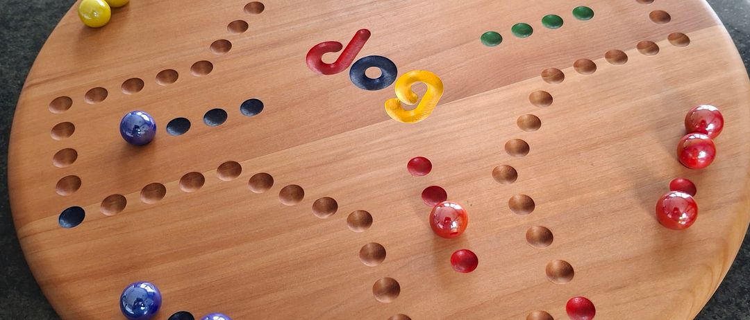 A wooden Catan board game on a countertop with colorful dice and marbles scattered on it. A box of Catan is visible in the background.