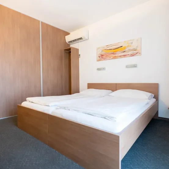 Ein ordentlich eingerichtetes Schlafzimmer mit zwei Einzelbetten, Holzkopfteilen und einer weißen Wand, die mit einem Gemälde und einer Klimaanlage verziert ist.