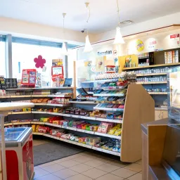 Ein gut sortierter Convenience-Shop mit verschiedenen Produkten im Angebot, darunter Snacks, Getränke und andere Artikel. Der Laden hat ein modernes Design mit gefliesten Böden und einem hellen Innenraum.