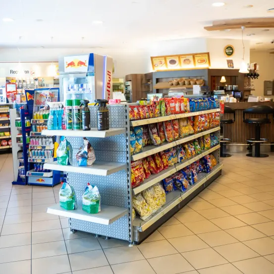 Ein Convenience-Store mit einer Auswahl an Snacks, Getränken und Reinigungsmitteln. Der Laden hat ein modernes Design mit weißen gefliesten Böden und einem gut beleuchteten Innenraum.