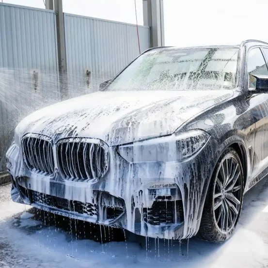 Ein BMW X5 SUV wird mit einem Hochdruckwasserstrahl in einer Autowaschanlage gereinigt. Das Fahrzeug ist mit Seifenwasser und Eistropfen bedeckt.