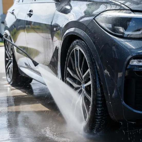 Ein schwarzer BMW SUV wird mit einem Hochdruck-Wassersprüher gereinigt, wobei der Fokus auf dem vorderen Rad und Reifen liegt.
