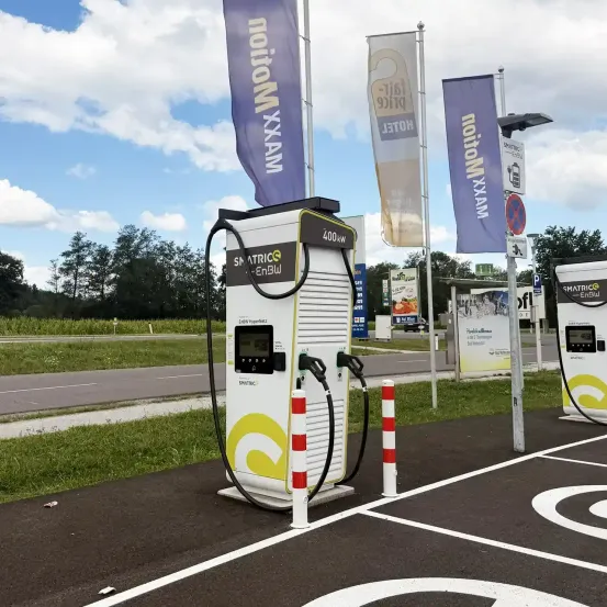 Zwei Elektroauto-Ladestationen sind am Straßenrand aufgestellt, mit Bannern und Schildern im Hintergrund.