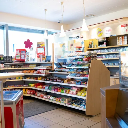 Ein gut bestückter Convenience-Shop mit verschiedenen Produkten zur Schau, einschließlich Snacks, Getränken und anderen Artikeln. Der Laden hat ein modernes Design mit weißen Wänden und gefliesten Böden.