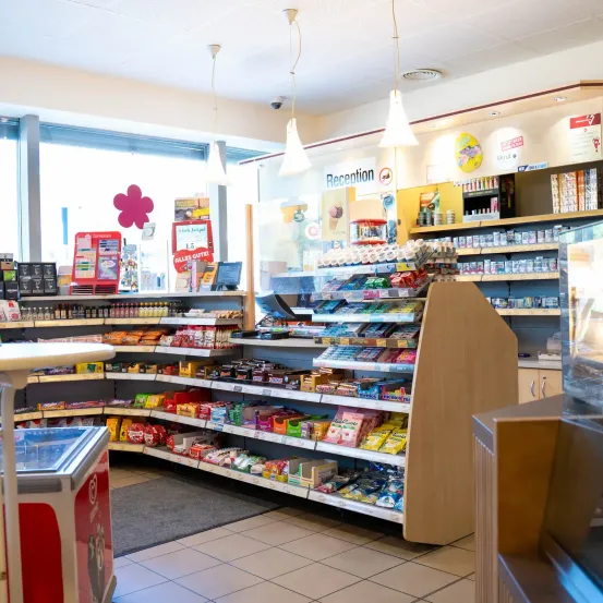 Ein gut bestückter Convenience-Shop mit verschiedenen Produkten zur Schau, einschließlich Snacks, Getränken und anderen Artikeln. Der Laden hat ein modernes Design mit weißen Wänden und gefliesten Böden.