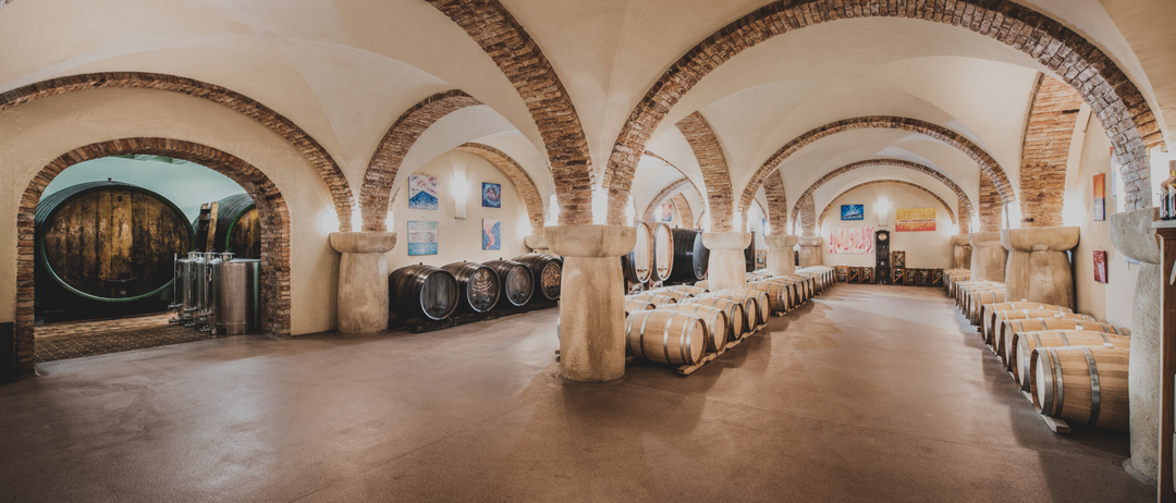 Ein Weingut mit Reihen von Fässern unter gewölbten Decken, mit Gemälden an den Wänden und Säulen.