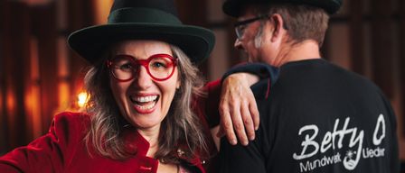 Two people are standing close together, smiling. The woman is wearing a red coat and a black hat, and the man is wearing a black hat and glasses. They seem to be at a wine event. The date is June 24.
