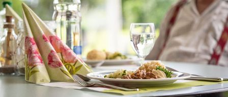 Ein gedeckter Tisch mit Essen, einem Glas Wasser und einer Flasche. Eine Person sitzt im Hintergrund.