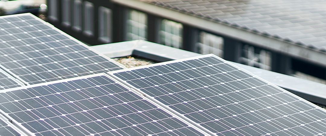 Nahaufnahme mehrerer Solarpanele auf einem Dach mit einem Gebäude im Hintergrund.