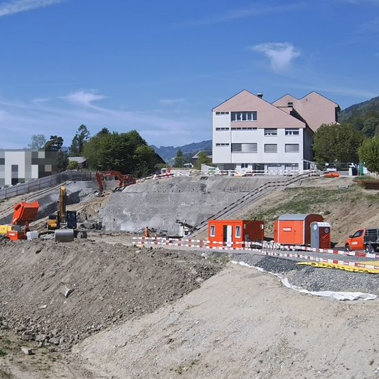 Baustelle mit Maschinen, ein Gebäude im Hintergrund und ein klarer blauer Himmel.