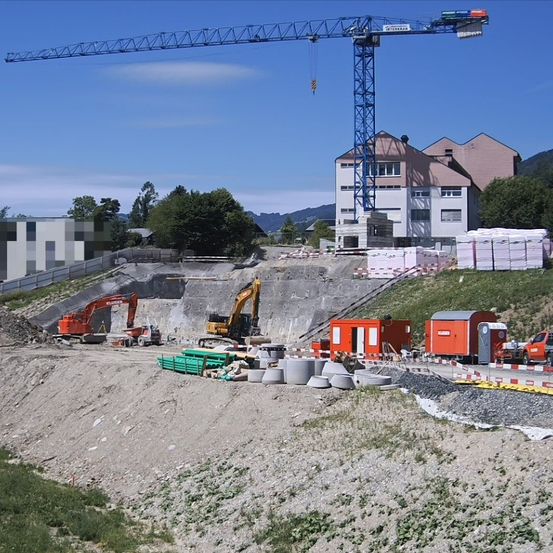 Eine Baustelle mit einem großen Kran, zwei Baggern, einem Haufen Material und einem kleinen Gebäude im Bau.