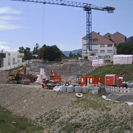 Eine Baustelle mit einem Kran, Baggern und Maschinenfahrzeugen. Ein Gebäude im Bau mit mehreren Räumen und Fenstern. Es gibt Sandhaufen und Lagerboxen.