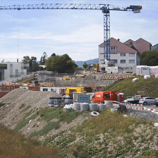 Eine Baustelle mit einem Kran, Fahrzeugen und Materialien. Im Hintergrund befindet sich ein Gebäude im Bau.