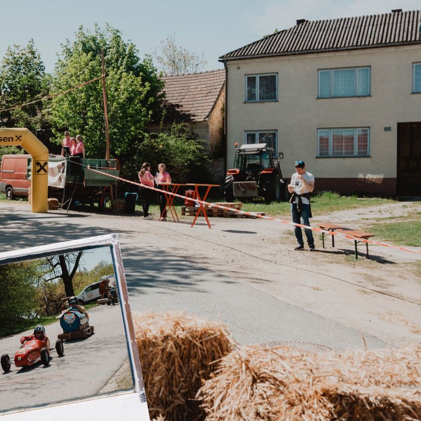 Ein kleines Go-Kart-Event mit Fahrern vor einem Haus und einem Traktor in der Nähe. Zuschauer beobachten von der Seitenlinie aus.