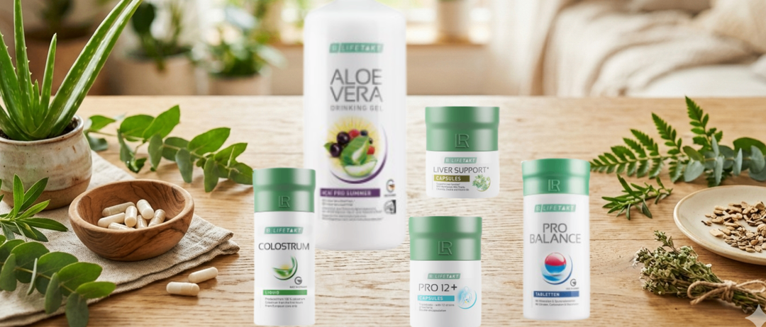 Eine Sammlung von Gesundheitsprodukten, einschließlich Aloe Vera Trinkgel, Colostrum Flüssig, Leberunterstützungskapseln und Pro Balance Tabletten, ist auf einem Holztisch ausgestellt.