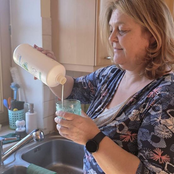 Eine Frau gießt Aloe Vera Lotion aus einer Flasche in ein Glas an der Küchenspüle.