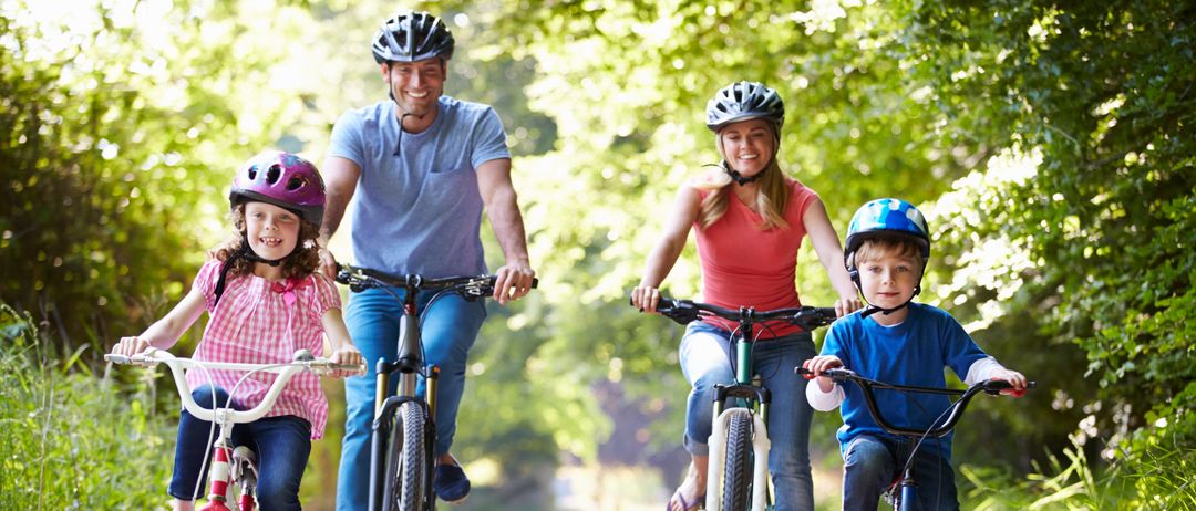 Eine vierköpfige Familie fährt auf einem Schotterweg. Ein Mann fährt mit einem kleinen Mädchen, während eine Frau mit einem Jungen fährt. Sie tragen alle Helme.