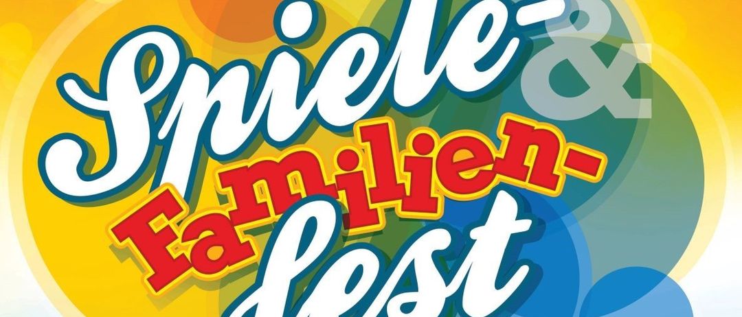 Das Bild zeigt den Text 'Spiele & Familien-Fest' in fetten, bunten Buchstaben vor einem mehrfarbigen Hintergrund. Das Design umfasst verschiedene überlappende Kreise in Gelb, Orange, Grün und Blau.