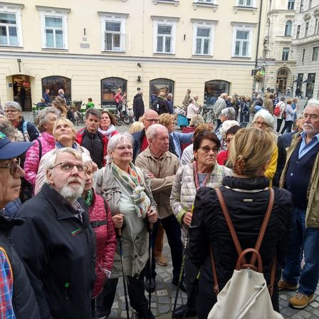 Eine Gruppe von Menschen ist an einem Außenort versammelt, einige tragen Brillen und haben Rucksäcke dabei. Sie stehen vor einem Gebäude, vor dem Fahrräder geparkt sind.