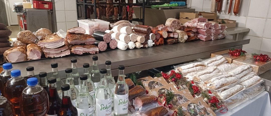 Ein Fleischtresen zeigt verschiedene Wurst- und Schinkensorten. Vorne stehen Flaschen mit Spirituosen und Ahornsirup. Regale und Gestelle halten weitere Fleischprodukte, und die Wände sind mit hängenden Wurstwaren geschmückt.