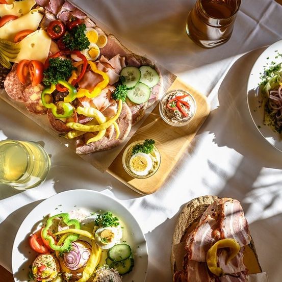 Ein Tisch mit verschiedenen Speisen: eine Charcuterie-Platte mit Fleisch, Käse und Gemüse, ein Salat mit Eiern und Speck und eine kleine Schüssel mit Dip.