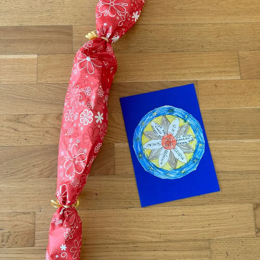 Eine rote Geschenkverpackung mit Blumendesigns und einer blauen Karte mit Blumendesign und fremdsprachigem Text auf einer hölzernen Oberfläche.