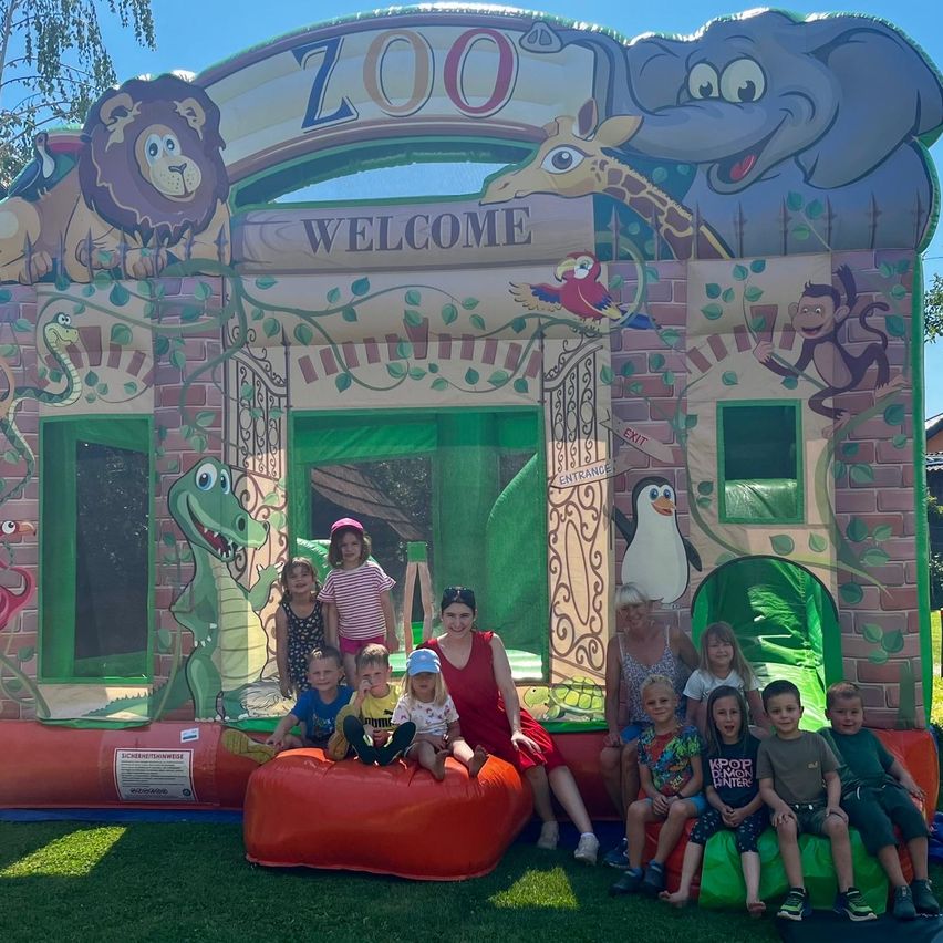 Eine Gruppe von Kindern und Erwachsenen posiert vor einem Zoo-Themen-Bouncer, mit Tieren an den Wänden und aufblasbaren Tieren auf dem Boden gemalt.
