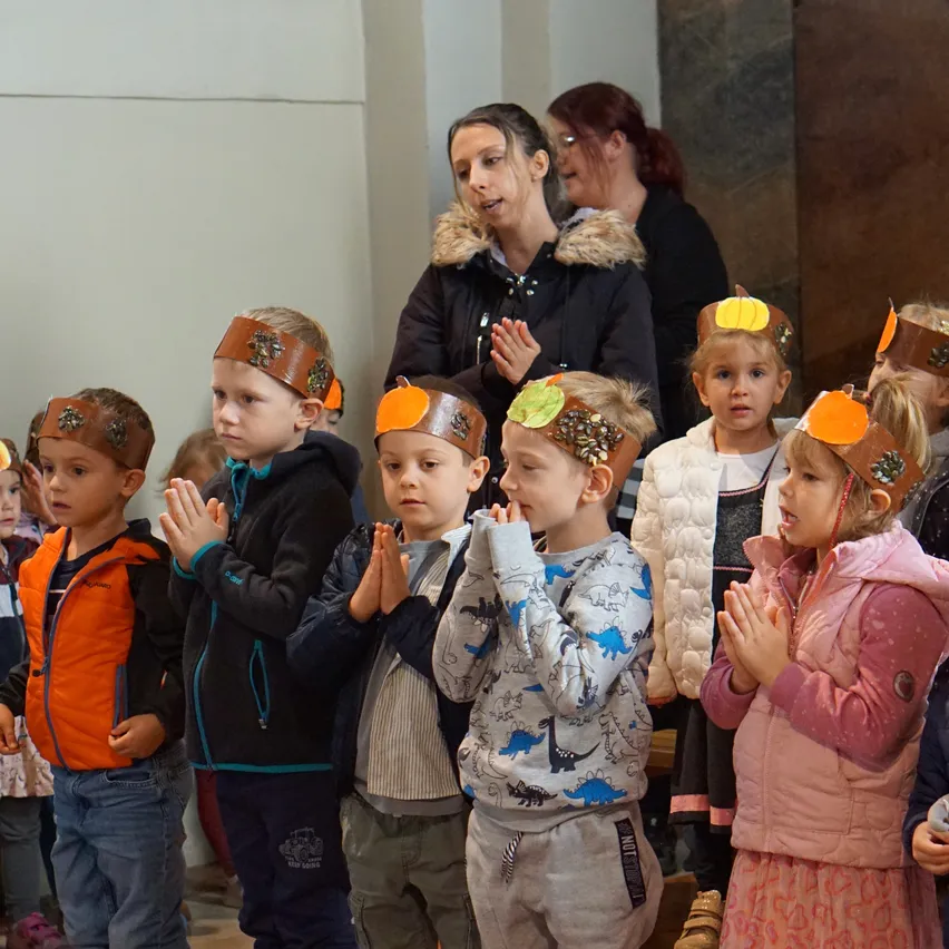 Eine Gruppe von Kindern mit Kopfbändern mit Kürbis-Designs steht in einer Reihe, wahrscheinlich in einer Kirche.