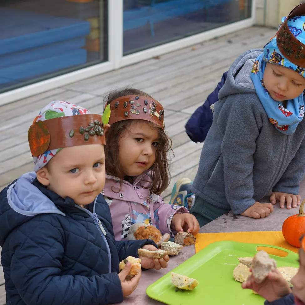 Vier Kinder sitzen um einen Tisch herum, tragen Kopfbänder und essen.