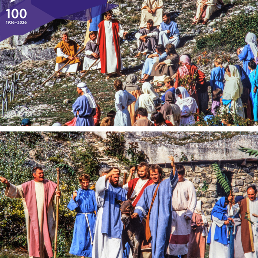 A group of people dressed in ancient attire, some standing and some sitting on a rocky surface. They seem to be in a meeting or gathering. They are surrounded by greenery. A donkey is standing in front of a group of people.
