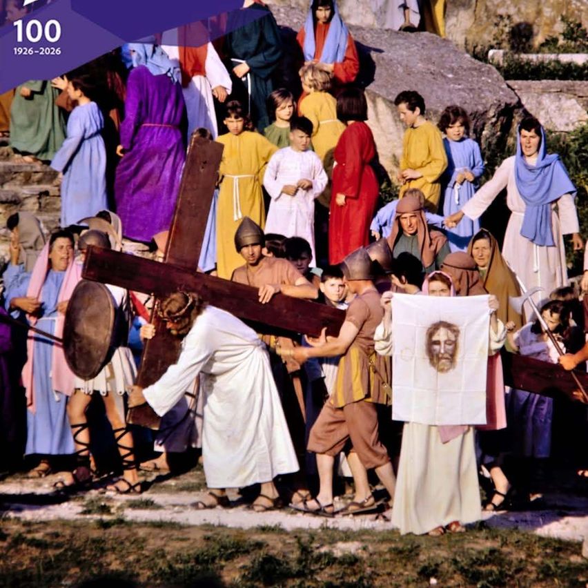 A reenactment of a biblical scene shows Jesus carrying a cross, with a large crowd of people in historical costumes watching.